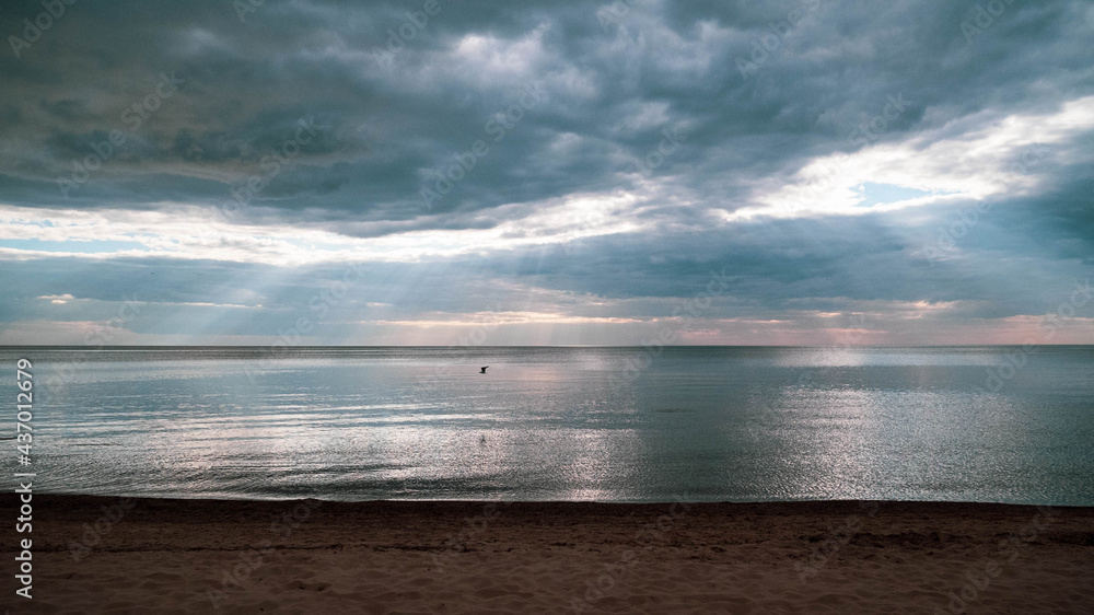 Calm sea on a summer evening with cloudy skies and sunbeams breaking through the clouds.