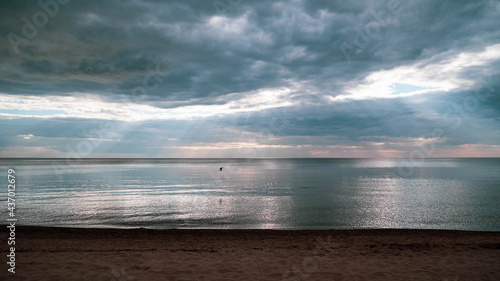 Calm sea on a summer evening with cloudy skies and sunbeams breaking through the clouds.