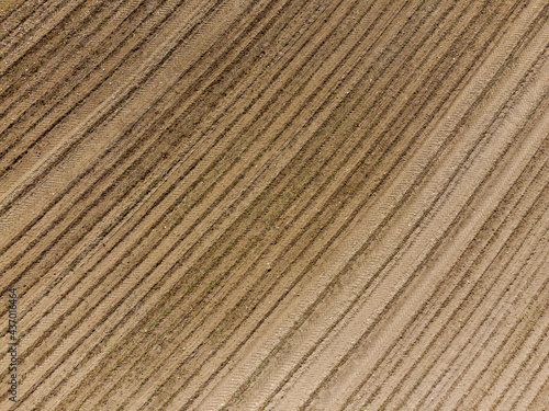 Aerial view down on empty barren field with very dry soil and plough furrows in bright sun light