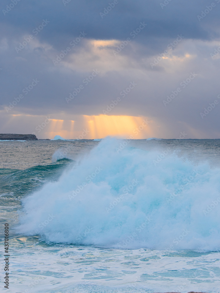 Ray of light over the wave breaking on the coast.