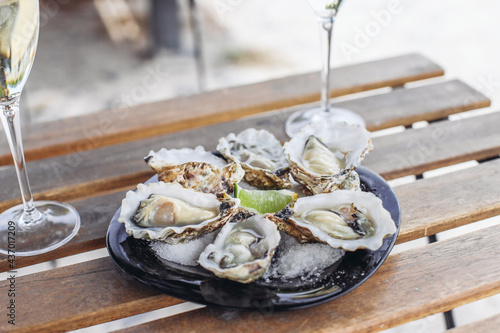 A plate of 6 oysters with lime, two glasses of sparkling wine on a wooden table in an outdoor cafe