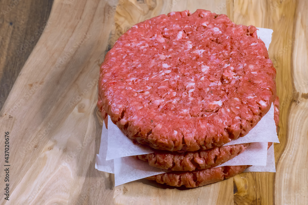 Stack of three fresh uncooked beef burgers separated with cooking paper on a cutting wooden board and table. Food industry. Stack of three fresh uncooked beef burgers separated with cooking paper on a cutting wooden board and table. Food industry.