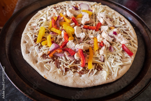 Frozen pizza with chicken pieces, red and yellow peppers ready to be cooked. Fast food concept. Retail industry product