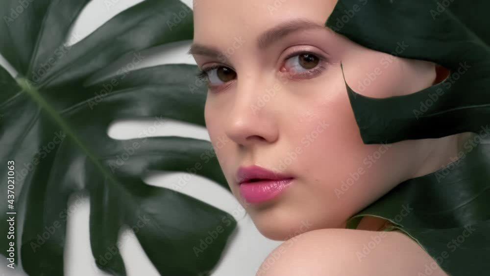 Closeup face of young beautiful woman with a healthy clean skin. Beautiful white girl with big green leaves. Beauty and spa treatment concept. Pretty woman with natural makeup and plant near face. Closeup face of young beautiful woman with a healthy clean skin. Beautiful white girl with big green leaves. Beauty and spa treatment concept. Pretty woman with natural makeup and plant near face.