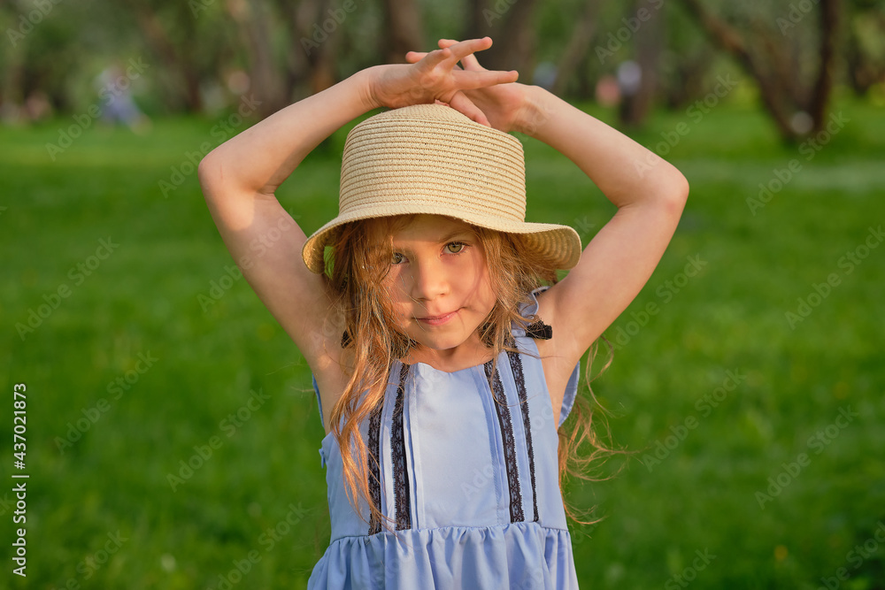 portrait of a young smiling girl, beautiful child outside in a straw hat enjoying a warm day