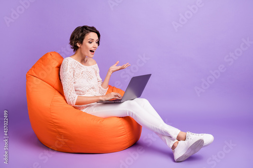 Full size profile portrait of positive person sitting soft chair speak video chat isolated on purple color background
