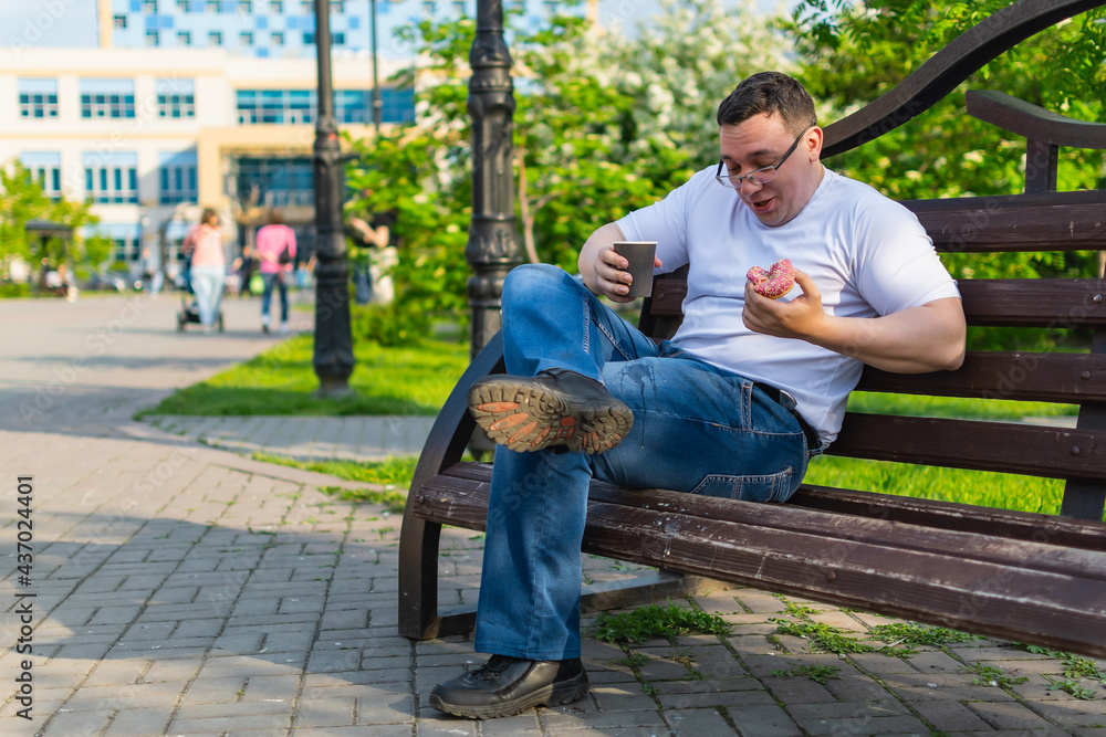 Fototapeta premium A young man in white sitting on a park bench accidentally spills hot coffee on his pants during lunch