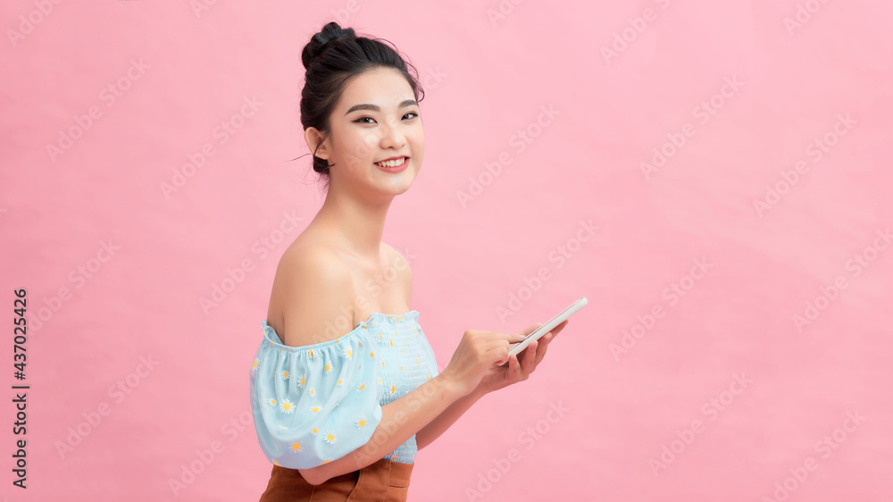Examining her brand new smart phone. Beautiful young women holding smart phone and smiling while standing against pink background Examining her brand new smart phone. Beautiful young women holding smart phone and smiling while standing against pink background