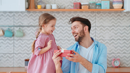 Cute little girl giving a gift to dad for a holiday in the living room. One parent with a child at home