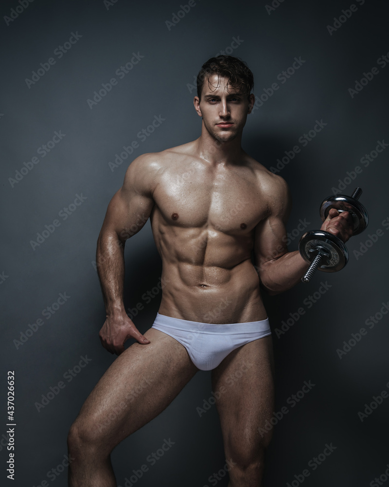 Muscular young man in white underwear with dumbbell in studio at grey background Muscular young man in white underwear with dumbbell in studio at grey background