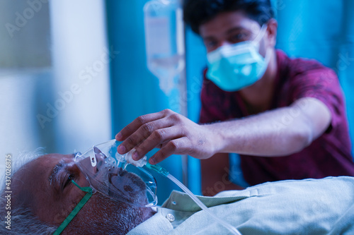 Fotografía Son with medical face mask taking care of sick old father at hospital by checking ventilator oxygen mask - concept of senior people parental health care and medical
