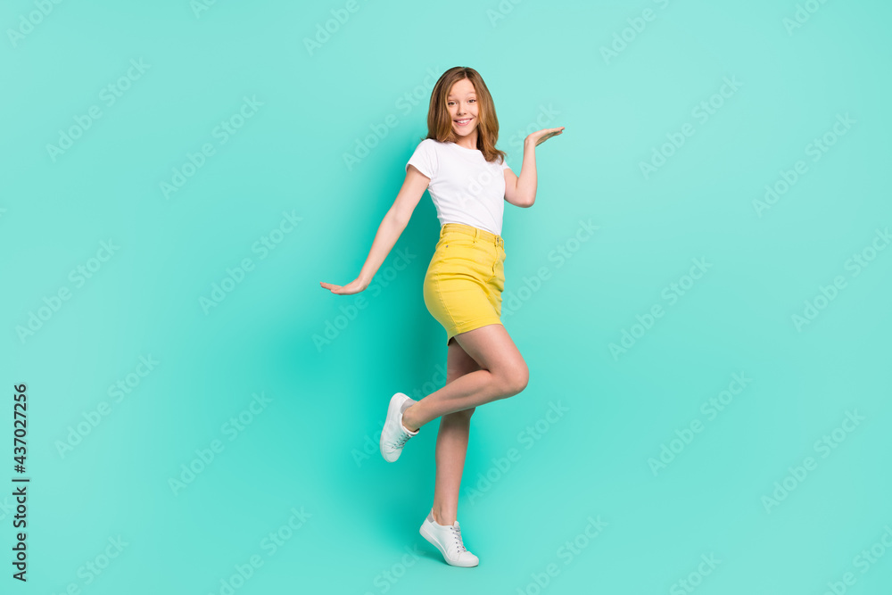 Full length body size photo smiling schoolgirl keeping copyspace on hand isolated vivid teal color background
