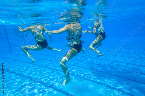 Synchronized Swimming Girls Team Unrecognizable Dance Underwater photography closeup action in blue pool water. 