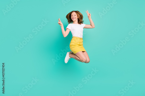 Full length body size photo smiling schoolgirl jumping up showing v-sign isolated vivid teal color background