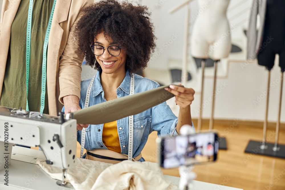 Woman boss checks sleeve sewed by young African-American seamstress in fashion studio Woman boss checks sleeve sewed by young African-American seamstress in fashion studio