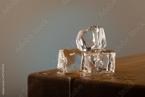 3 blocks of ice melting on a oak table, with a blue shined background on a grey surface. With dipping water from the table.