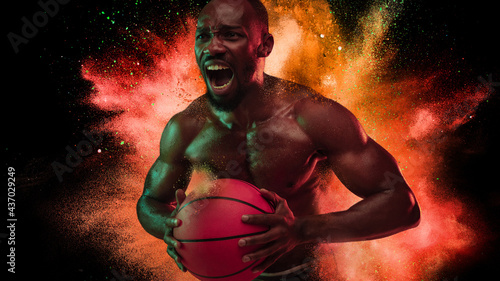 One young African sportsman basketball player in explosion of colored neon powder isolated on black background