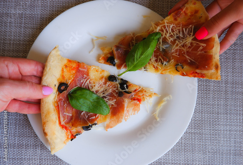 Close-up top view of a female hand takes a slice of pizza from a white plate. Appetizing delicious pizza.
