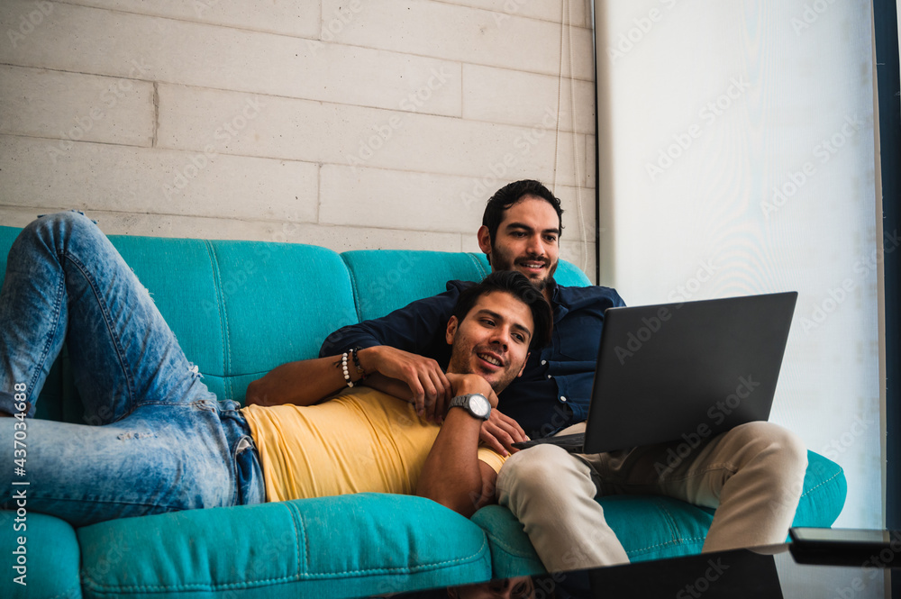 Ethnic gays sharing laptop while resting on couch at home Ethnic gays sharing laptop while resting on couch at home