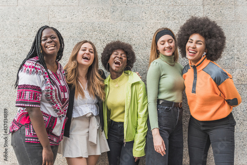 Confident multiracial girlfriends in casual wear against wall