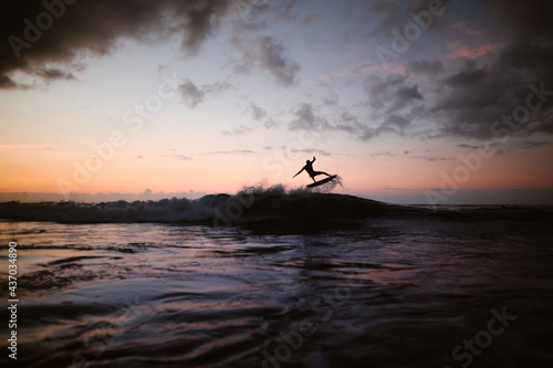 Unrecognizable athlete practicing surfing on ocean wave at sunset