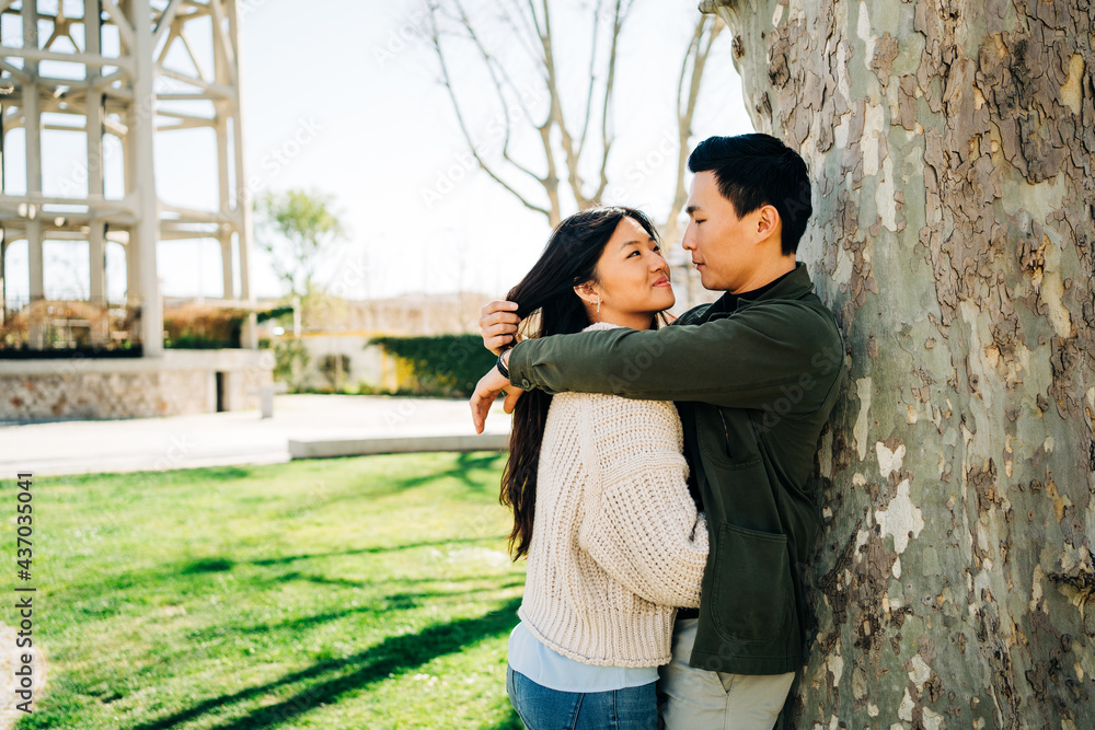 Enamored young Asian couple embracing near tree in park Enamored young Asian couple embracing near tree in park