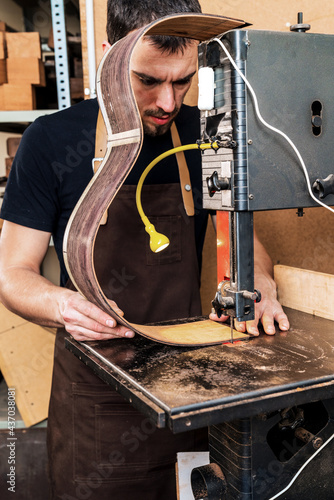 Crop luthier cutting guitar body on bandsaw in workroom photo