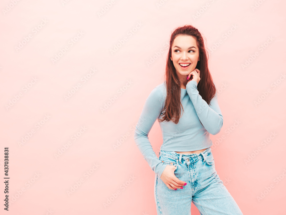 Obraz premium Young beautiful smiling female in trendy summer hipster clothes. Sexy carefree woman posing near light blue wall in studio. Positive model having fun indoors. Cheerful and happy