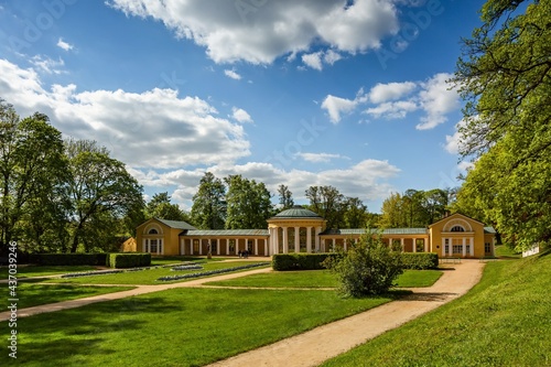Fototapeta Naklejka Na Ścianę i Meble -  Marianske Lazne, Czech Republic - June 1 2021: The Ferdinand spring pavilion, a yellow building, standing in a park with green lawn and trees. Sunny day with blue sky and clouds.