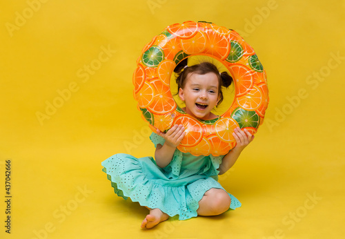 fun little girl plays with an inflatable swimming circle on a yellow background with a copy of the space