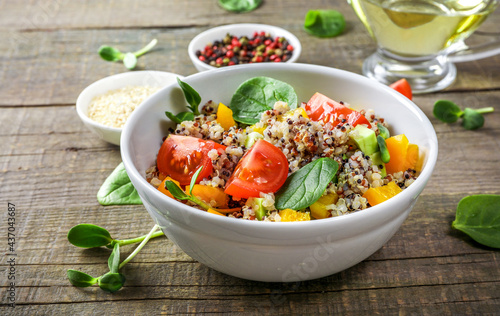 Quinoa salad with tomatoes, batata and spinach on wooden background. Vegan food concept.