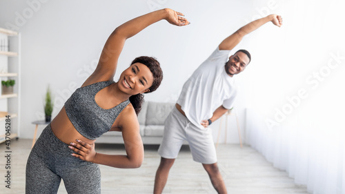 Foto Millennial black couple doing lateral flexion exercise, working out together at