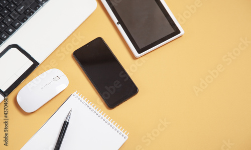 White laptop computer, smartphone, notepad, pen, tablet and mouse on yellow background.