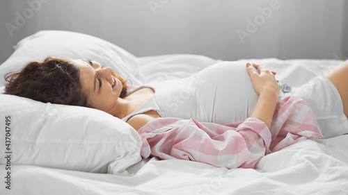 happy young woman touching belly while lying in bed