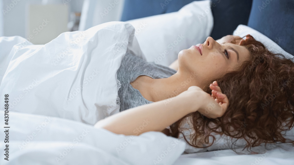 young curly woman lying on bed in morning young curly woman lying on bed in morning