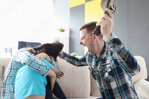 Angry man yells at his wife and child holding belt in his hand photo