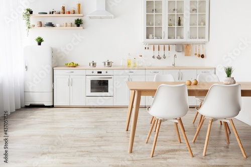 Light kitchen design in scandinavian style. Wooden dining table and white furniture, small refrigerator, empty space