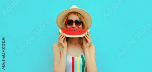 Summer portrait of happy smiling young woman with slice of watermelon wearing a hat on blue background