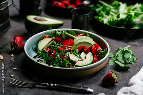 Salad with strawberries, avocado and arugula in a plate on the table. Vegetarian salad