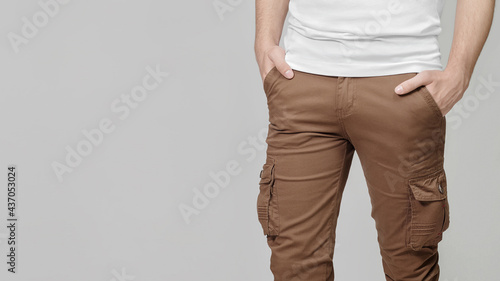Εκτύπωση καμβά Model wearing brown cargo pants with hands in pockets on grey background, empty place for text on the left