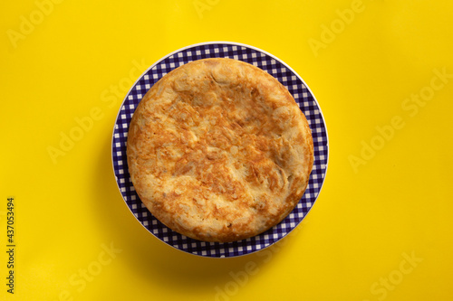 Tortilla de Patatas española. Delicioso plato salado basado en Huevo, Patatas y a veces Cebolla. En fondo amarillo, entera y sin cortar. 