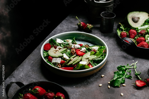 Salad with strawberries, feta, avocado and arugula in a plate on the table. Vegetarian salad