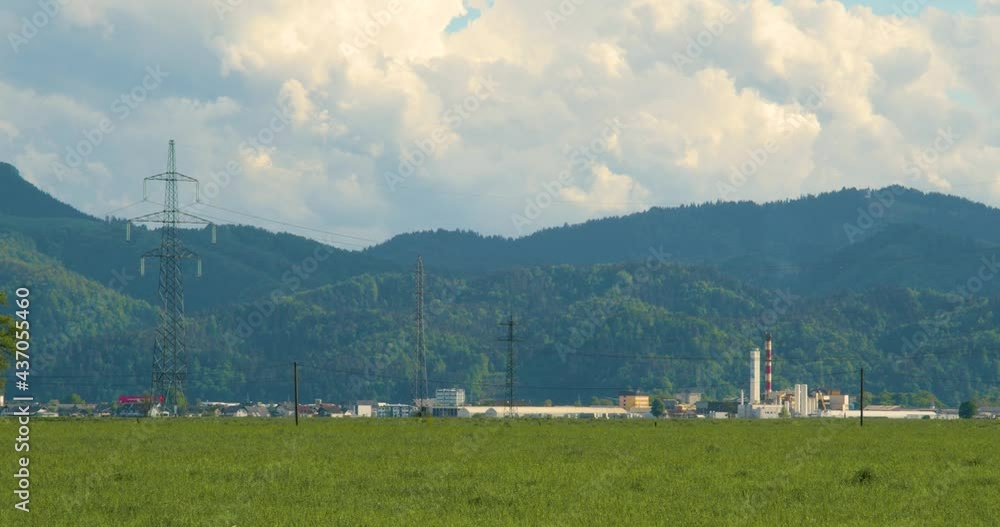 Factory in the countryside with hills in the background. Green farmland in Slovenia. Wide angle, left pan, real time Factory in the countryside with hills in the background. Green farmland in Slovenia. Wide angle, left pan, real time