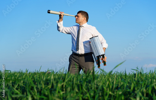 businessman poses with a spyglass in a green field, he looks an idea or something, business concept, green grass and blue sky as background