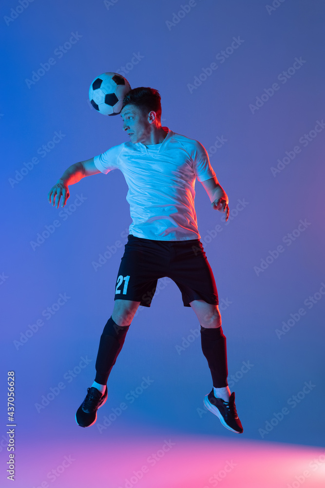 Young Caucasian man, male soccer football player jumping isolated on gradient blue pink background in neon light. Back view
