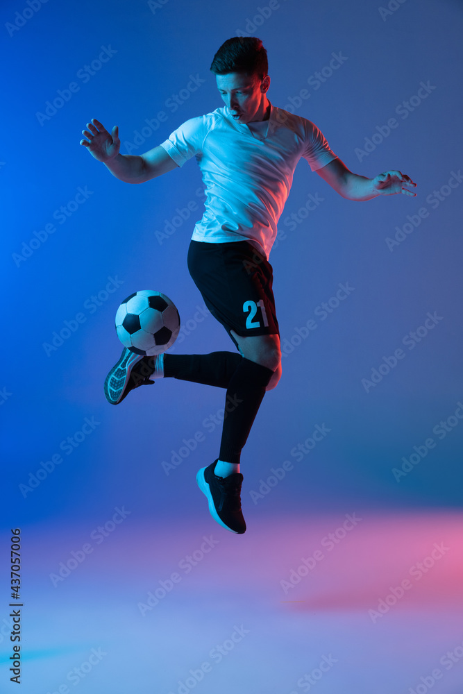 One male soccer football player in action and motion isolated on gradient blue pink background in neon light One male soccer football player in action and motion isolated on gradient blue pink background in neon light