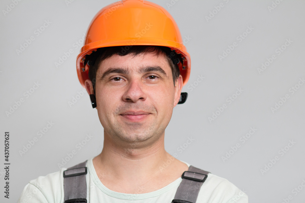 portrait of successful and happy construction worker in a helmet, face of young foreman on gray background