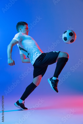 Fototapeta Naklejka Na Ścianę i Meble -  Young Caucasian man, male soccer football player training isolated on gradient blue pink background in neon light