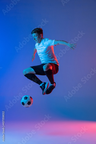 Young Caucasian man, male soccer football player training isolated on gradient blue pink background in neon light © master1305