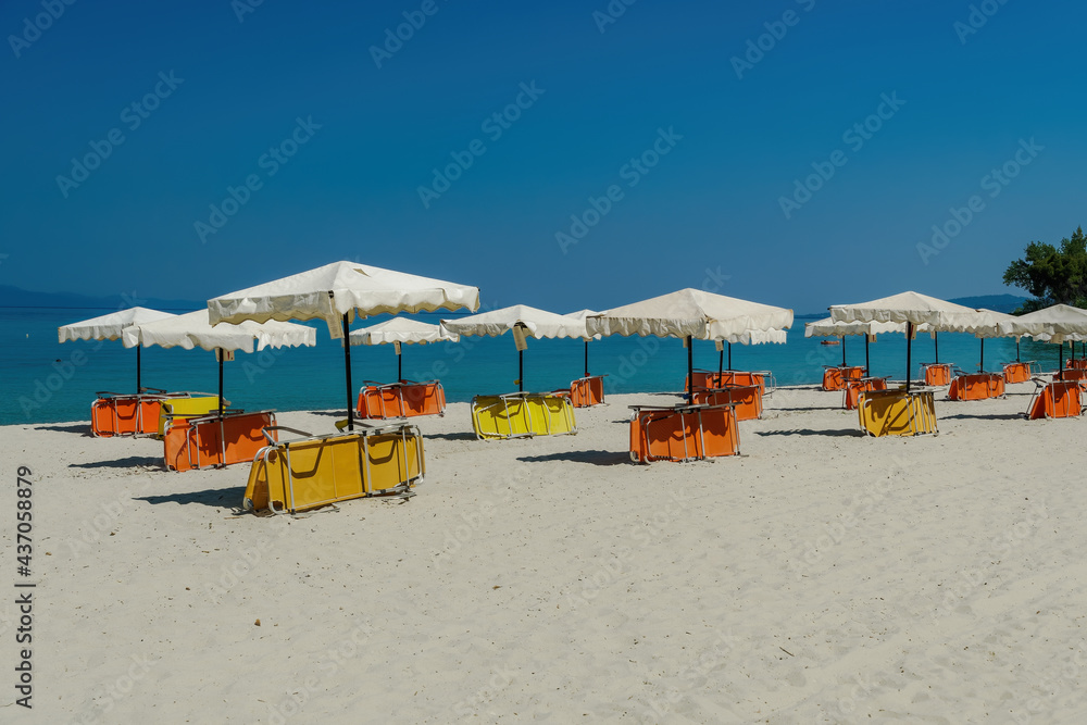 Beach beds under sun umbrellas on an empty sandy beach in Chalkidiki Peninsula, Greece